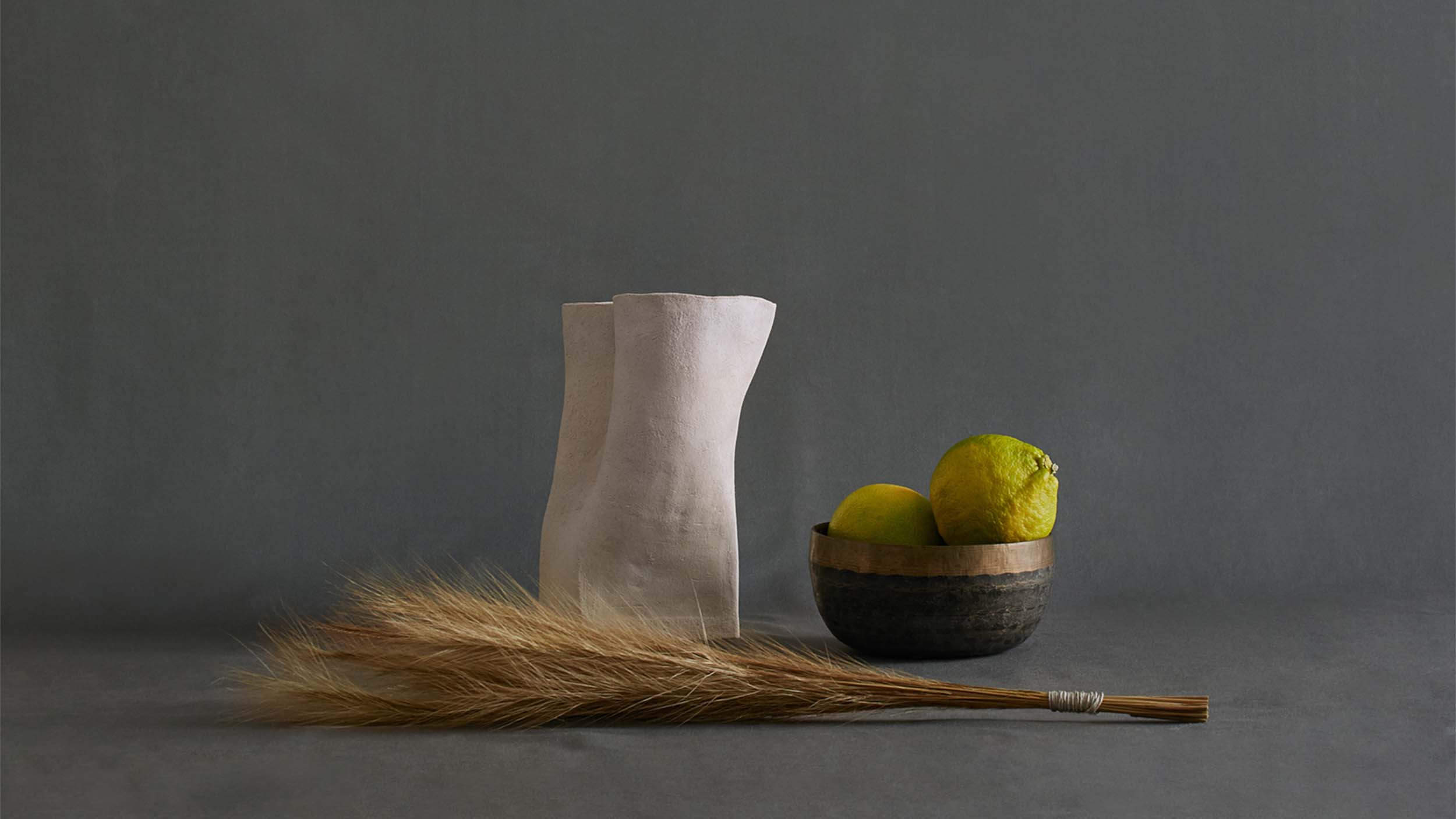 White ceramic vessel, with bergamots in rustic brass bowl and bunch of dried grass